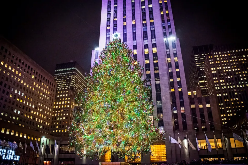 View of Rockefeller Center Christmas tree lit up at night in front of 30 Rock high-rise.